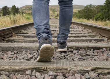 Bulutlu bir günde kırsal kesimde tren raylarında yürüyen tanınmayan genç adam ayakları.