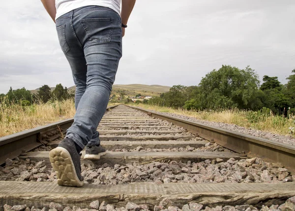 Jovem irreconhecível caminhando nas trilhas ferroviárias em uma cena rural em um dia nublado — Fotografia de Stock