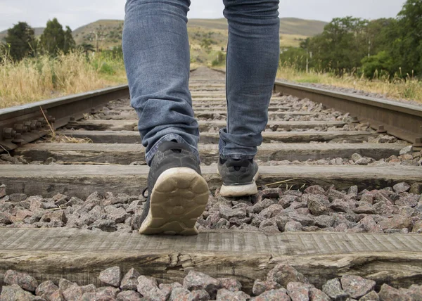 Unrecognizable young man feet walking on the railway tracks in a rural scene in a cloudy day