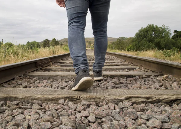 Unrecognizable young man feet walking on the railway tracks in a rural scene in a cloudy day
