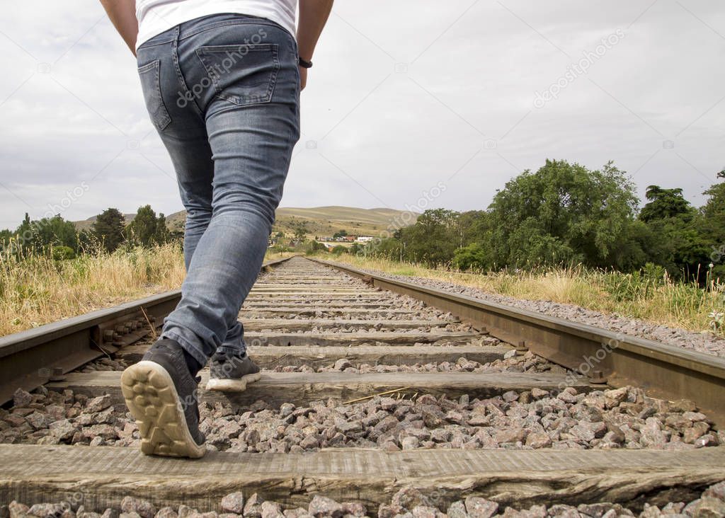 Unrecognizable young man walking on the railway tracks in a rural scene in a cloudy day