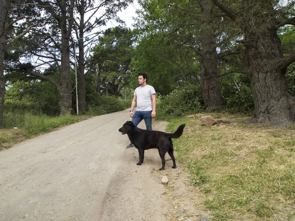 Молодой человек с чёрным псом-лабрадором, оба смотрят в сторону — стоковое фото