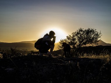 Dağdaki fotoğrafçı silueti büyük bir köpeğe fotoğraf çekiyor. Gün batımında veya gündoğumunda manzaraya ateş ediyor.