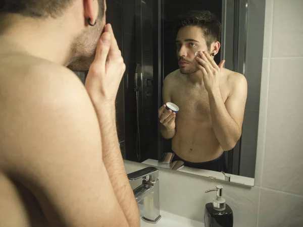 Portrét hezkého kavkazského teenagerského odrazu ze zrcadla, nanášení hydratačního krému na obličej — Stock fotografie