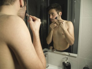 Aynadan yansıyan yakışıklı beyaz çocuk portresi, jiletle tıraş oluyor.