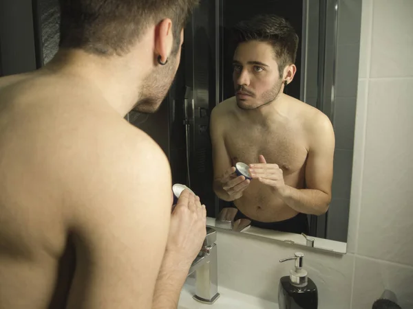Potret remaja tampan Kaukasia refleksi dari cermin, menerapkan krim wajah pelembab — Stok Foto