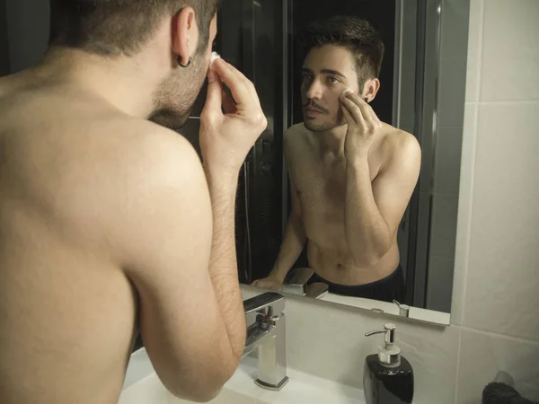 Retrato de guapo caucásico adolescente reflexión desde el espejo, la limpieza de su cara con algodón removedores de maquillaje — Foto de Stock