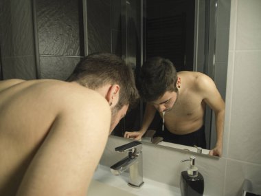 Portrait of handsome caucasian teenager reflection in from of the mirror, spitting after rinse his mouth