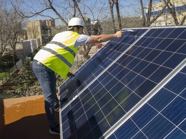 Beyaz tenli genç teknisyen cam silecekle güneş panellerini temizliyor. Alternatif elektrik kaynağı, sürdürülebilir kaynak kavramı.