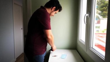 Genç beyaz bir adam evinden çıkmaya hazırlanıyor cüzdanını, anahtarlarını alıyor ve tıbbi maske takıyor. Yeni normallik kavramı.