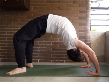 Genç yakışıklı beyaz adam yoga, briç ya da tekerlek yogası yapıyor. Ev konsepti alıştırması.