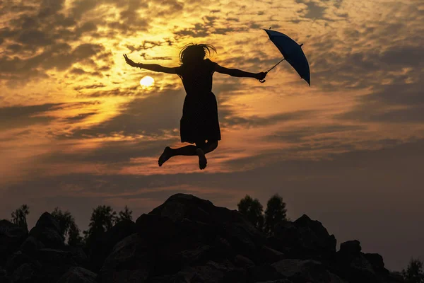 Silhouette şemsiye kadın atlama ve Günbatımı ile büyük güneş, peyzaj.