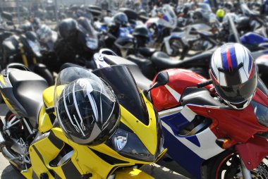 Park yerinde benzer iki motosiklet yarışı standı. Kaskın asılı olduğu bir motosikletin gidonunda. Arka planda motosikletler var..