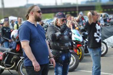 İki göbekli motorcu siyah gözlük takıyor. Uzun saçları ve sakalları isyanı süslüyor. Motosikletlilerden biri sigara içiyor..