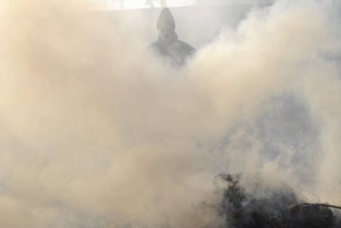 Dumanın içindeki adam. Ellerinde tırmık var. Etrafta çok duman var..