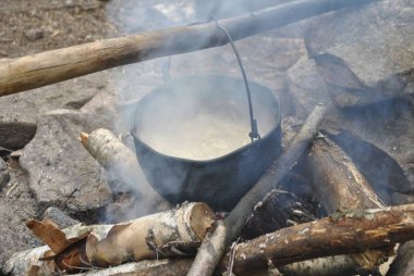 Kazan ateşin üzerinde asılıdır. Kazan bir sopaya asılı..
