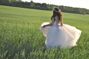 Buğday tarlasında fotoğraf çekiminde gelin. Gelin gelinliği içinde dönüyor. Gelin bir gelinlik alıyor. Güneş ışınları gelini aydınlatır. Gelinin gölgesi yeşil alana düşüyor..