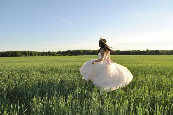 The bride at the photo shoot. The bride is spinning in her wedding dress. Bride in the field. The sun\'s rays illuminate the bride. The bride\'s shadow falls on the green field. Forest in the background.