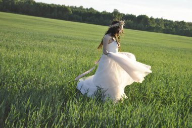 Gelin buğday tarlasında dönüyor. Buğday tarlasında fotoğraf çekiminde gelin. Gelinliği gelin alır. Güneş ışınları gelini aydınlatır. Gelinin gölgesi yeşil alana düşüyor..