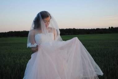 Buğday tarlasında fotoğraf çekiminde gelin. Gelin gelinliği gözleri kapalı kaldırır. Kafasına peçe takıyor..