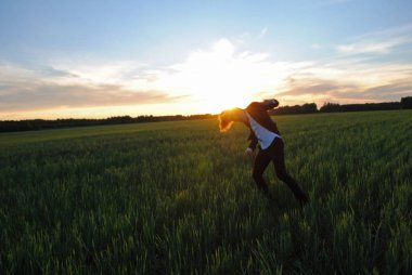 Ofis kıyafetli bir adam buğday tarlasında dans ediyor. Adam saçı açık başını sallıyor..