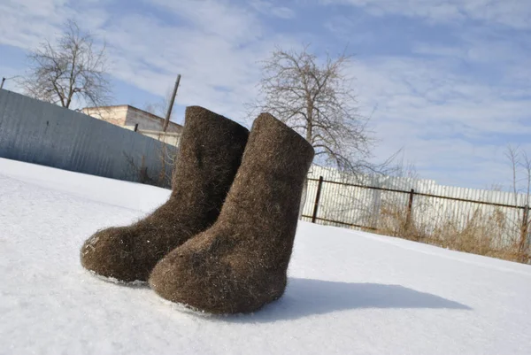 Brown felt boots. Snow stuck to the boots. Valenoks are covered with small ice floes. The shadow of the boots falls on the snow.