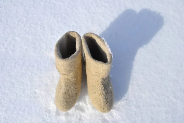 White boots stand in the snow. Boots top view. Valenoks are covered with small ice floes. Snow stuck to the boots. The shadow of the boots falls on the snow.