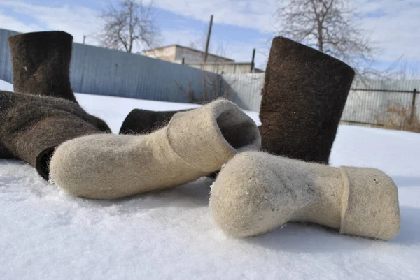 Three pairs of felt boots close-up. White and brown boots. Valenoks are covered with small ice floes. Snow stuck to the boots.