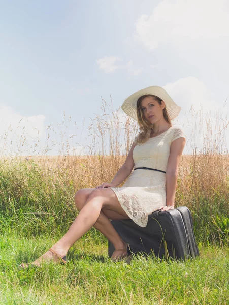Женщина сидит с чемоданом на краю поля — стоковое фото