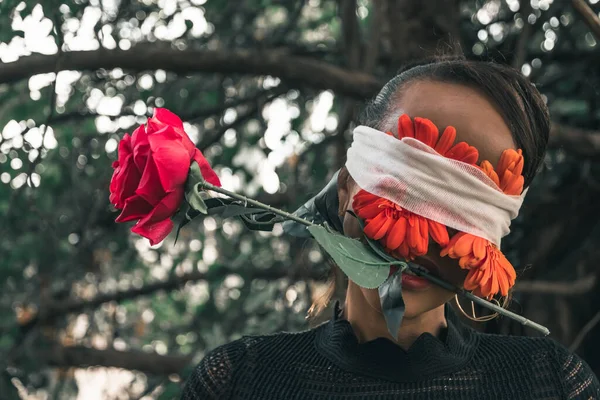 赤い口紅を身に着けている女性とフープイヤリングとともに赤い花包帯で彼女の目に彼女の口の中でバラ — ストック写真