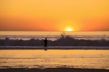 Balıkçı hloding olta kamışı batımında sahilde silüeti