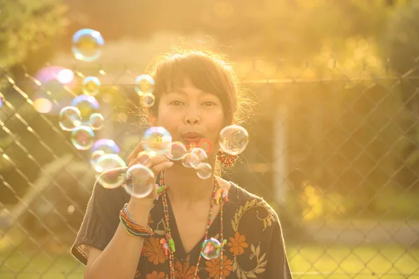 夏日黄昏时分 年轻美丽的亚洲女子在公园里吹肥皂泡的柔和焦点 老式风格 — 图库照片