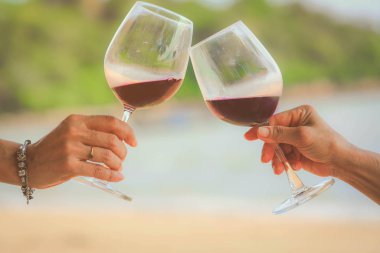 Sahilde kırmızı şarap kadehlerini tutarken yakın çekim, kutlama konsepti