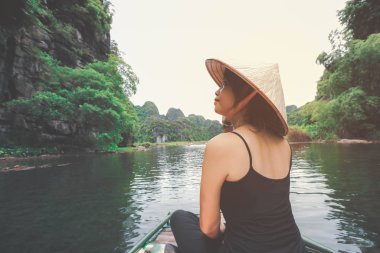 Ninh Binh, Vietnam 'daki tatili sırasında tahta teknede oturan Asyalı kadın.