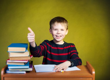 Mutlu çocuk başparmak, masada kitaplar ile ödev.