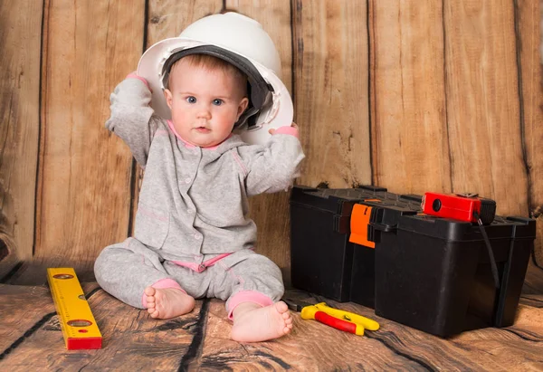 Funny cute baby in helmet playing with tools on wooden backgroun — Stock Photo, Image