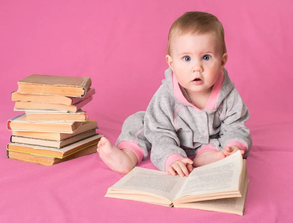 可爱的宝宝女孩与旧书在粉红色的背景上阅读。佛 图库图片