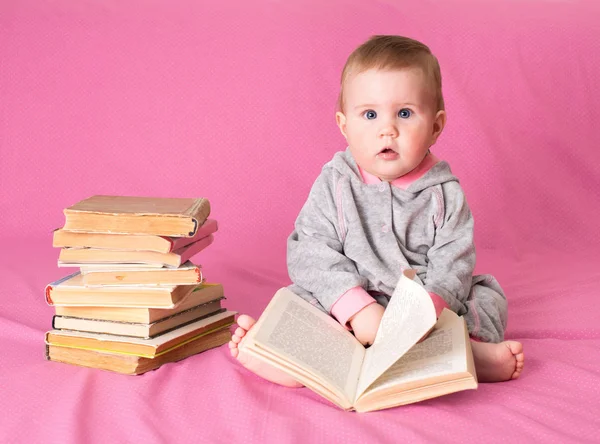 在粉红色的背景上阅读的老书的小女孩。热心 图库图片