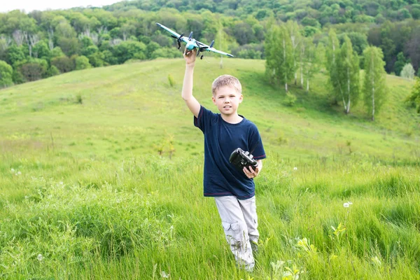 Niño feliz con avión en un prado en un día soleado. Sonriente joven preparándose para lanzar avión RC . — Foto de Stock