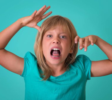 Küçük kız growls turkuaz arka plan üzerinde izole kızgın. Bir surat ve kameraya ekşitmeden çocuk portresi.