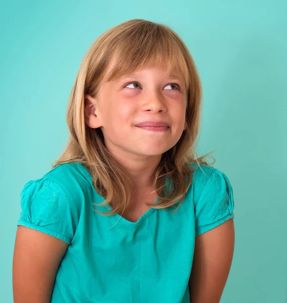 Linda niña astuta aislada sobre fondo turquesa. Emoción humana expresión facial . — Foto de Stock