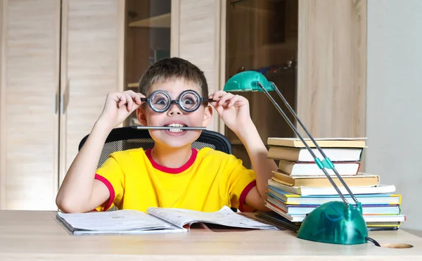 Um rapaz de óculos engraçados a fazer trabalhos de casa na mesa. Educação co — Fotografia de Stock