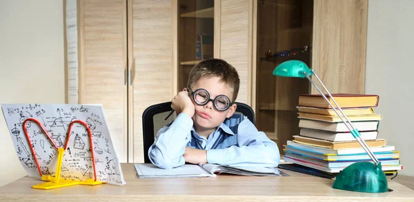 Müder Junge mit lustiger Brille bei den Hausaufgaben. Kind mit Lernschwierigkeiten Stockbild