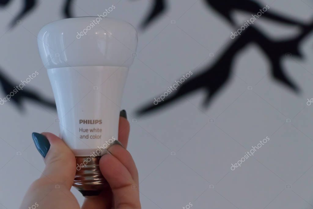 Vancouver, Canada - October 12, 2019: A Woman is holding Philips Hue Bulb in her  hand with white wall in the background