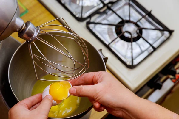 Woman breaks the egg into a mixer bowl and separating egg whites from egg yolks.