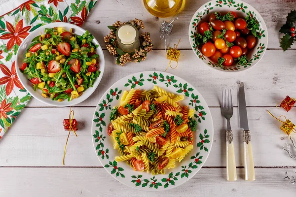 Christmas table. Green salad with strawberry and color pasta rotini. — Stock Photo, Image