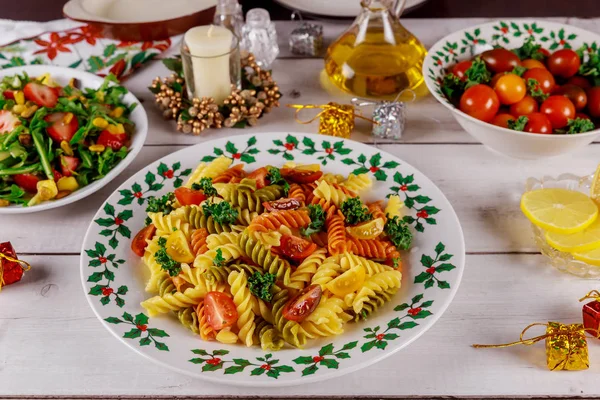 Festive christmas dinner with colorful pasta, cherry tomatoes, salad on white wooden table. — Stock Photo, Image