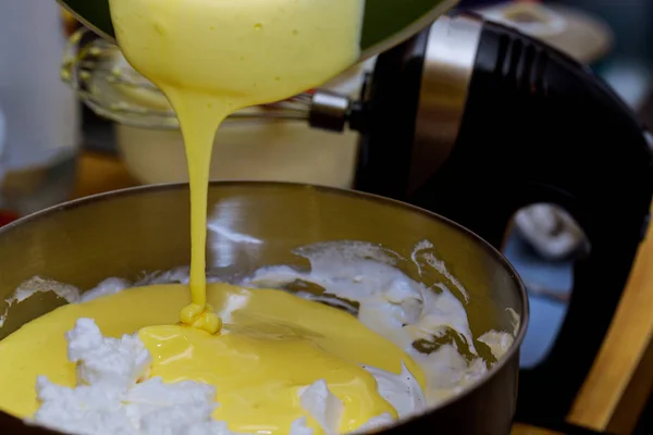 Pouring egg yolk into wipped egg white. Making fluffy dough. — Stock Photo, Image