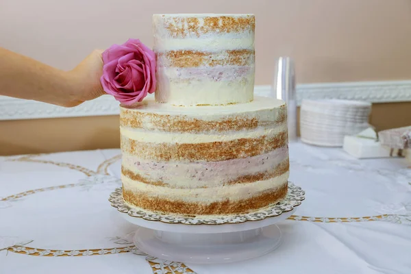 Frau legt Blume Rose auf stilvolle nackte Torte. Kuchendekoration. — Stockfoto