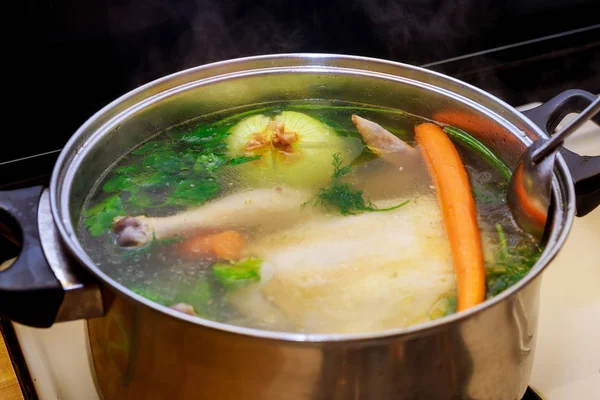 Chicken broth with carrots, whole chicken, onion, celery and parsley in steel pot. — Stock Photo, Image